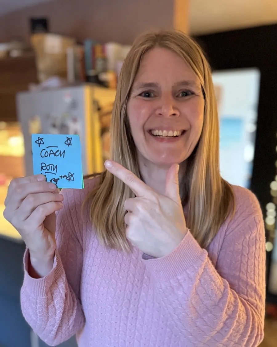 Ruth grinning and pointing at a sticky note that says Coach Ruth