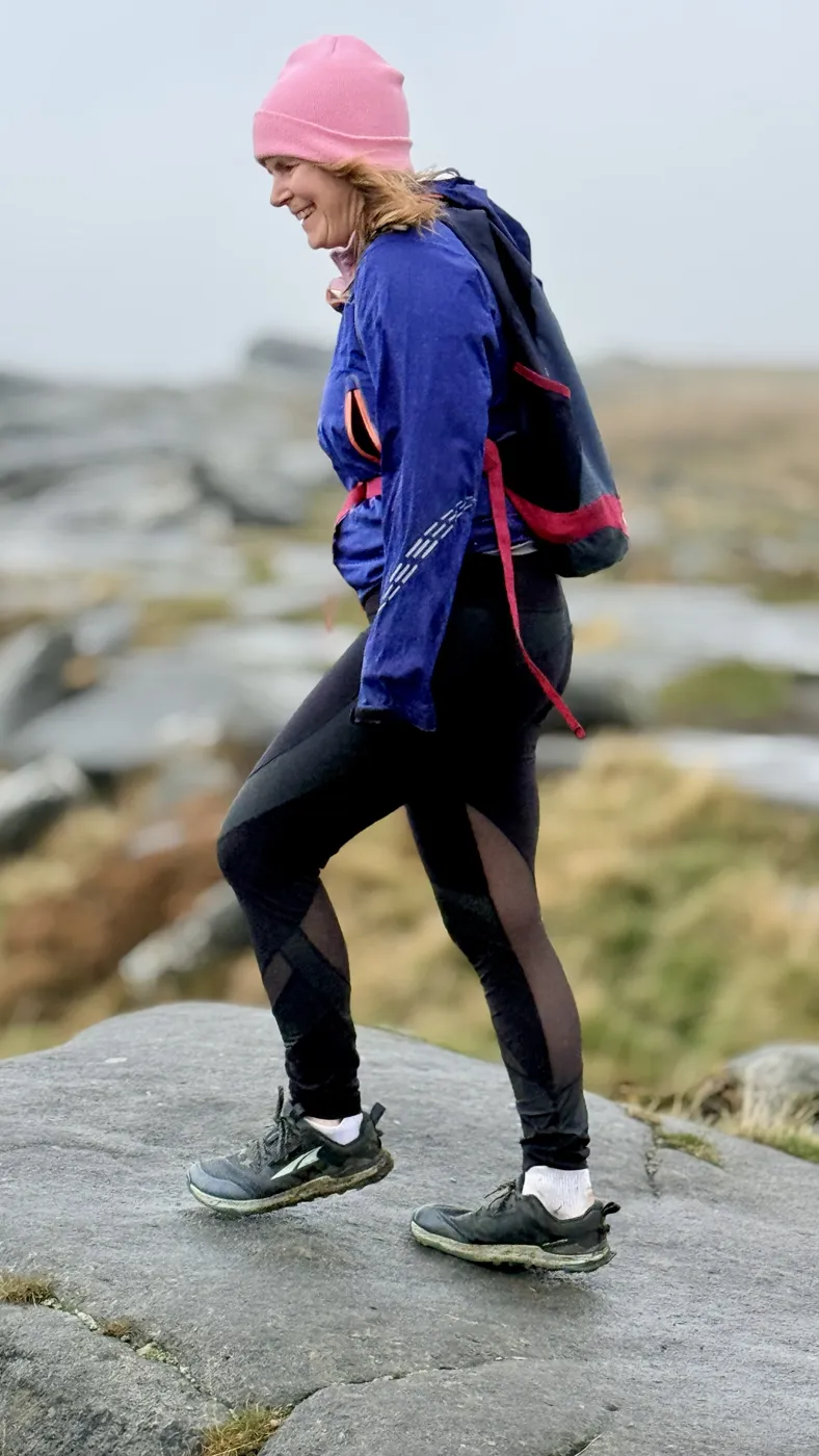 Ruth smiling as she steps forward across a rocky moorland ridge